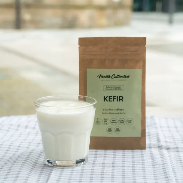 A glass of kefir placed on a checkered cloth, next to a branded Kefir starter culture.